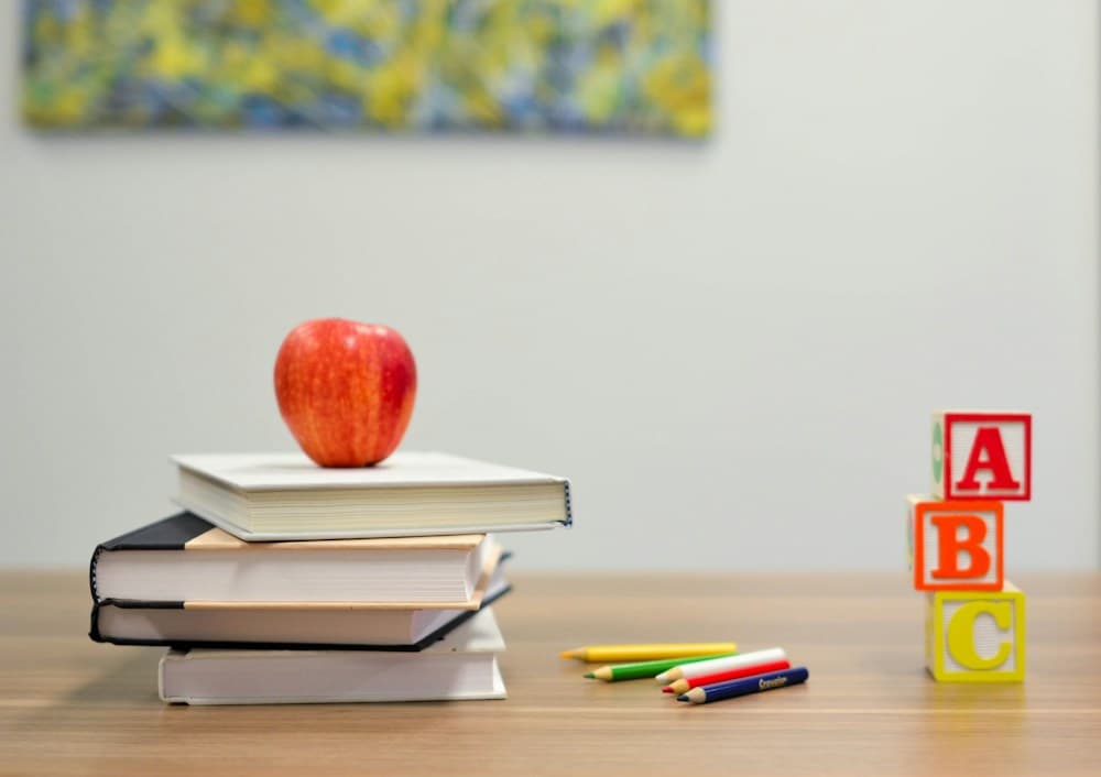 Books, colored pencils, an apple, and alphabet blocks on a classroom desk